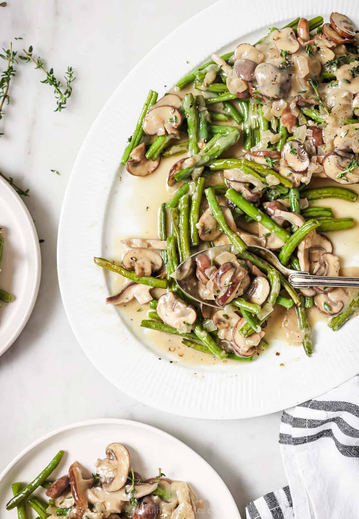 Angled photo of green beans and mushrooms with creamy lemon-thyme sauce on a serving platter. 