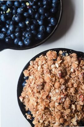 Blueberries inside of a skillet beside a skillet full of blueberry filling and pecan topping.