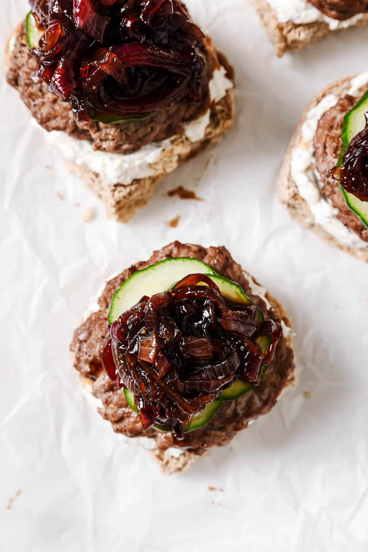 Assembling burgers with whipped feta, caramelized onions and cucumbers.