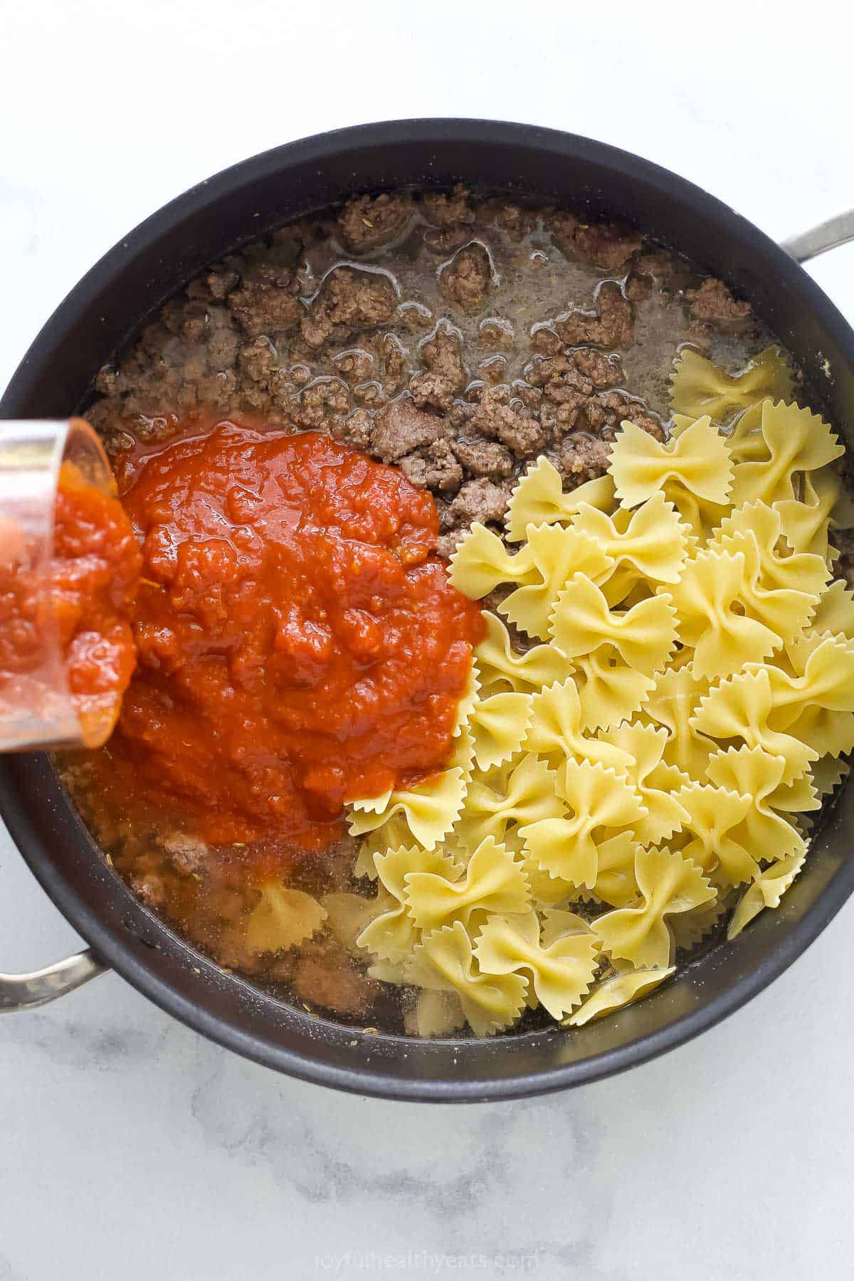 Adding the tomato sauce, pasta, and water to the ground beef. 