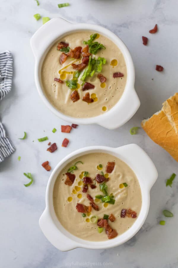 Two bowls of homemade cauliflower soup with bacon, green onions, and chili oil.