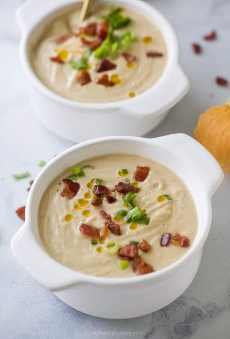 Two bowls of hearty cauliflower soup topped with bacon, green onions, and chili oil.