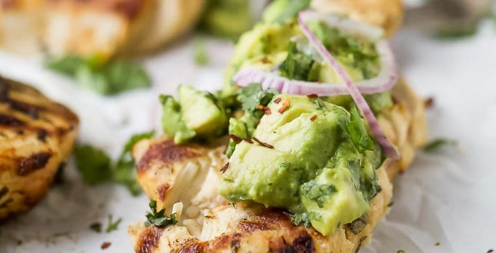 side photo of sliced grilled cilantro lime chicken topped with avocado salsa and red onion