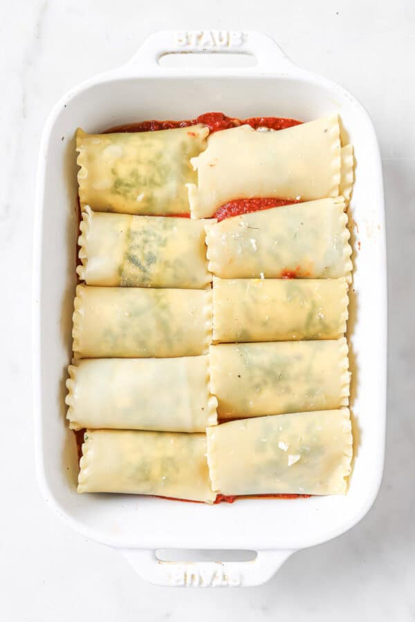 Lasagna sheets rolled with cheese on a baking tray with a layer of marinara sauce on the bottom. 