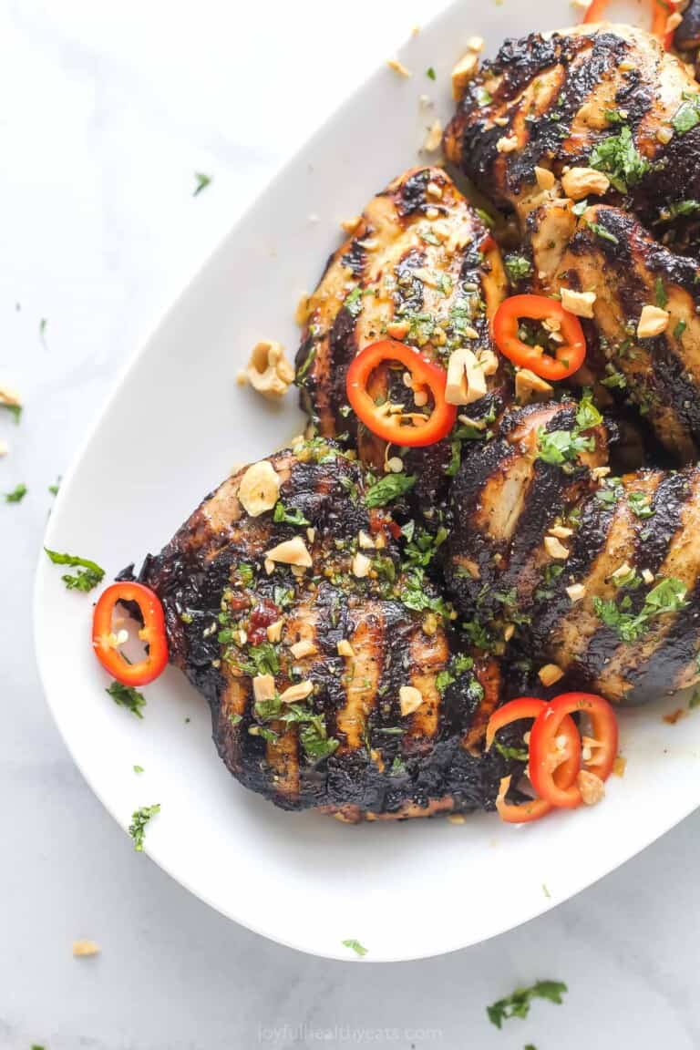 Angled photo of grilled Thai chicken with spicy chilis and chopped cashews.