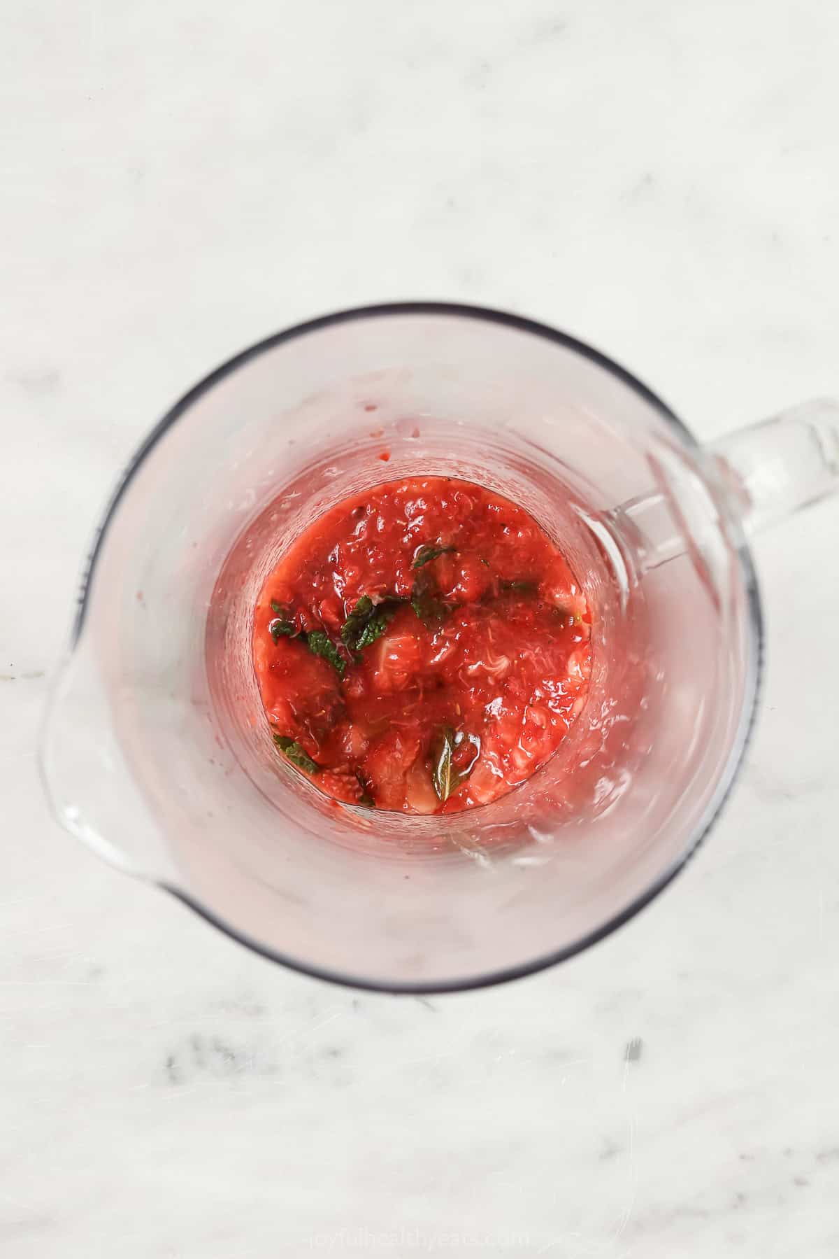 Muddled strawberries and mint in a small pitcher. 