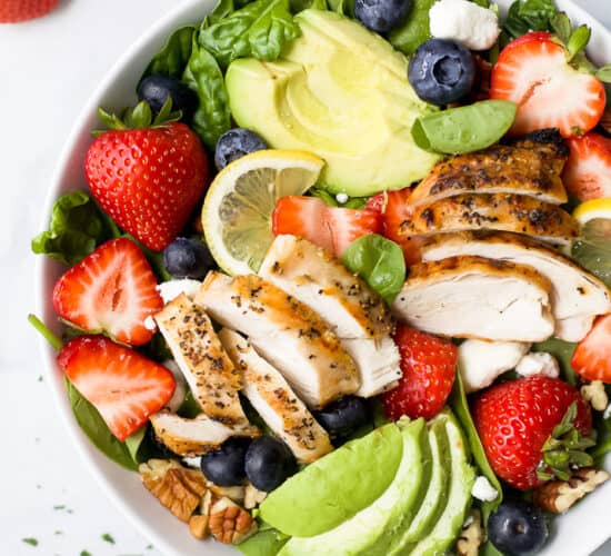 a bowl filled with best avocado strawberry salad with grilled chicken