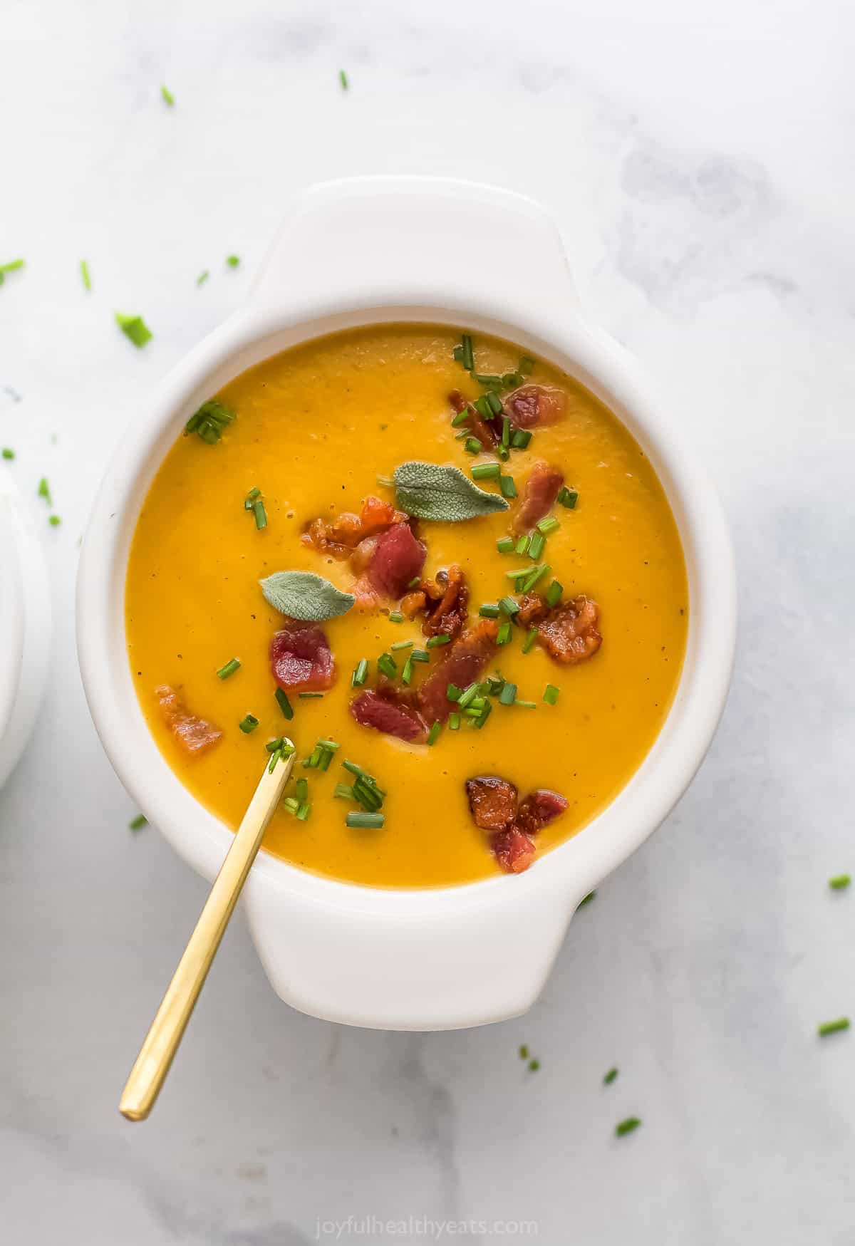 Bowl of butternut squash soup with crispy bacon and crunchy chives on top.