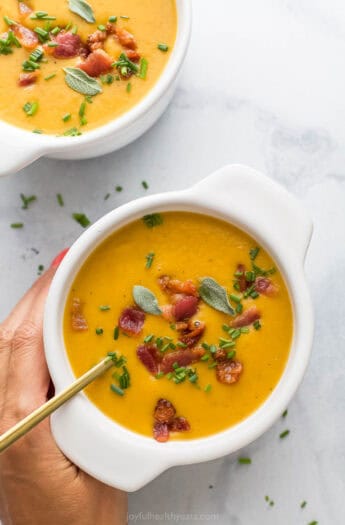 Grabbing a bowl of creamy butternut squash soup with bacon and chives on top.