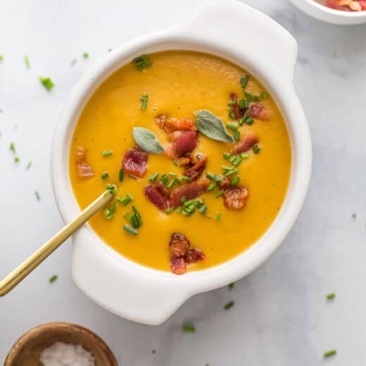 A bowl of silky, homemade squash-pepper soup with crunchy chives and smokey bacon.