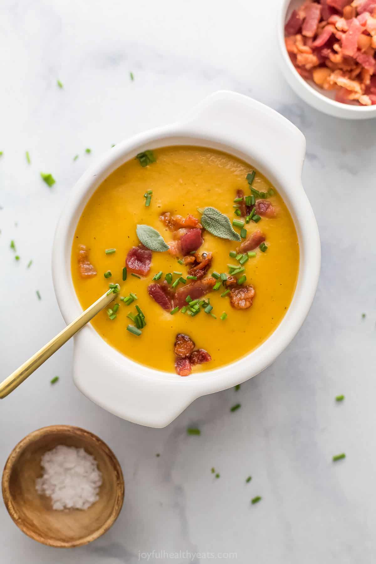 A bowl of silky, homemade squash-pepper soup with crunchy chives and smokey bacon.