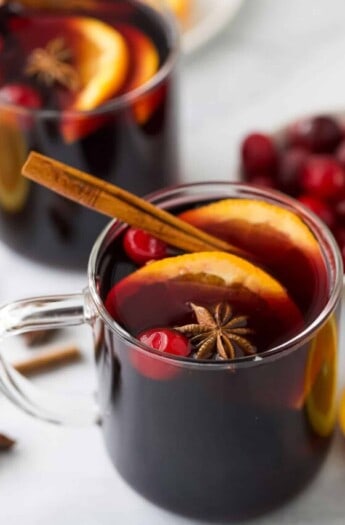 Glass of mulled wine recipe with orange slices and a cinnamon stick.