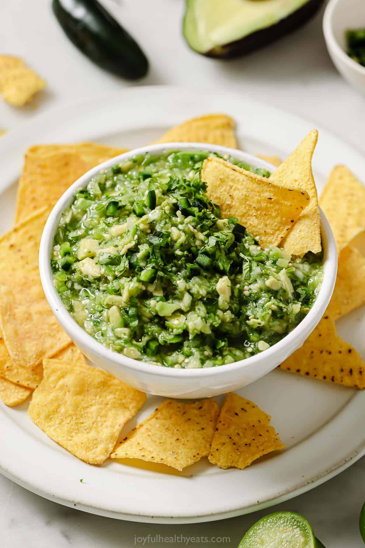 A bowl of chunky avocado salsa verde with tortilla chips on the side. 