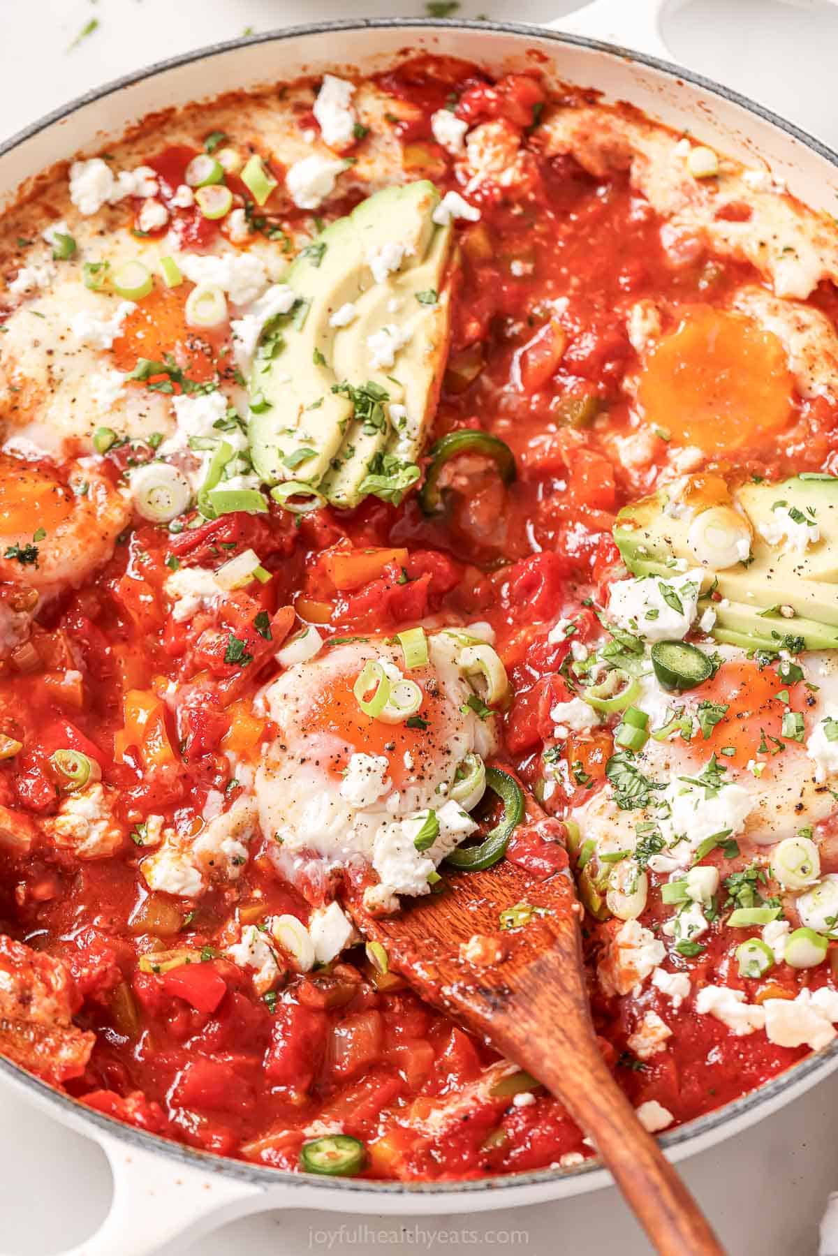 Digging a wooden spoon into the tomatoey shakshuka.