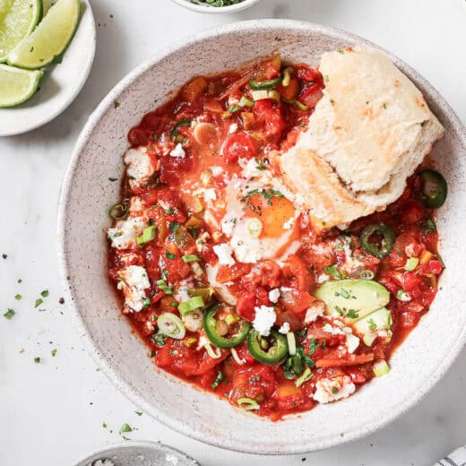 Landscape photo of one-skillet shakshuka with avocado, jalapeños, cilantro, and queso fresco on top.