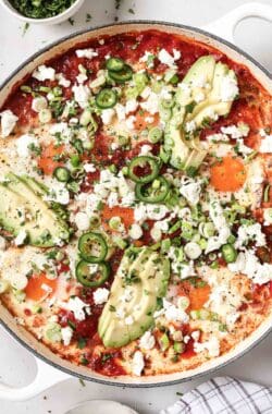 Freshly-made one-skillet shakshuka with queso fresco, cilantro, green onions, jalapeños, and creamy avocado on top.