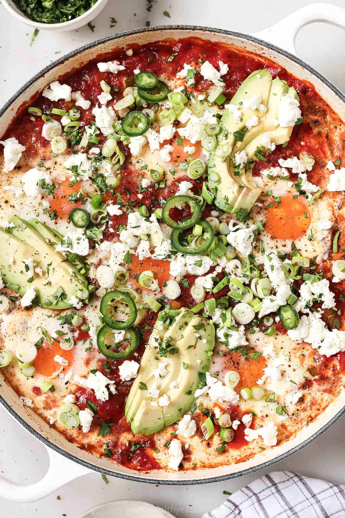 Freshly-made one-skillet shakshuka with queso fresco, cilantro, green onions, jalapeños, and creamy avocado on top. 