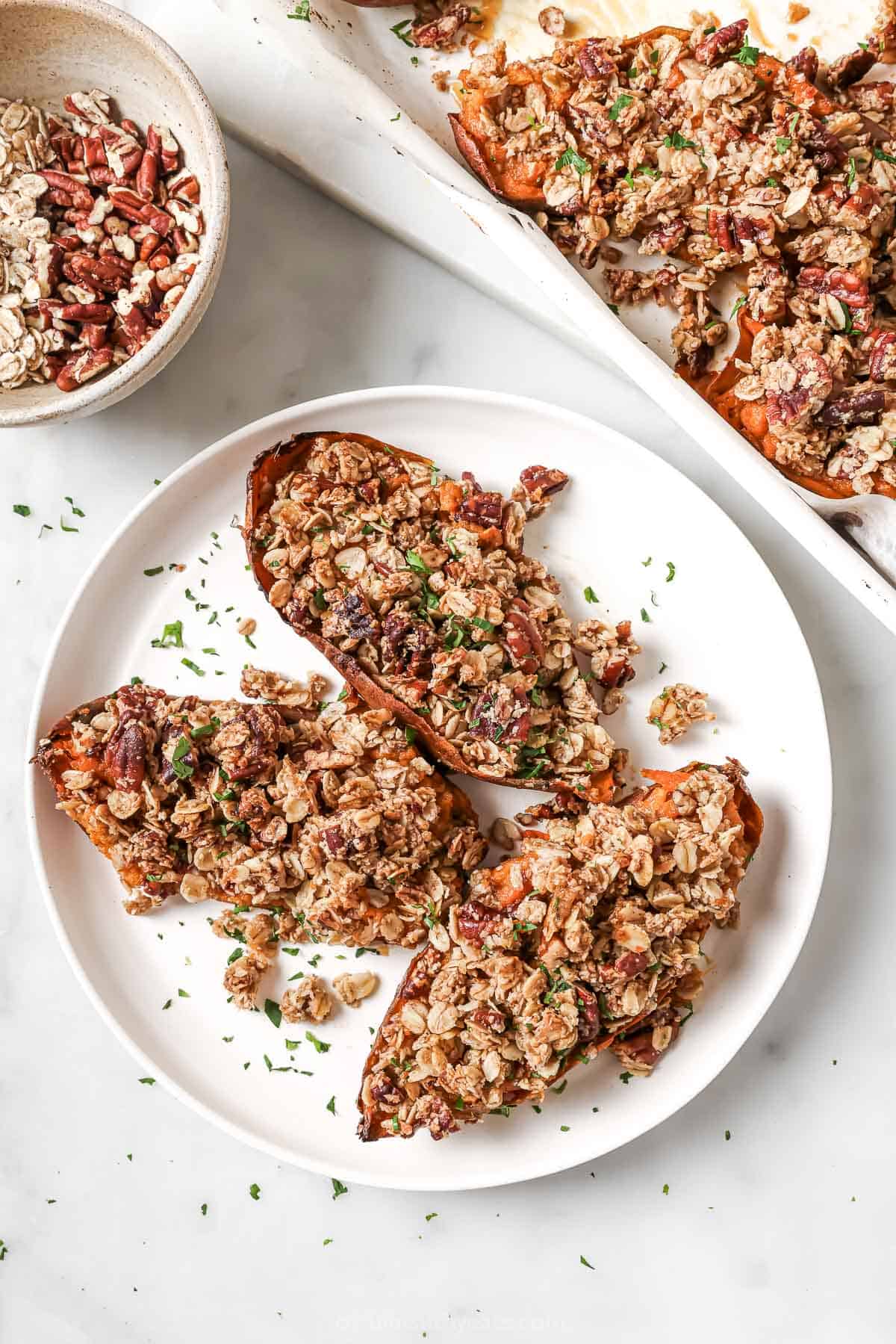 Baked sweet potatoes with maple syrup and streusel on a serving plate next to the baking sheet. 