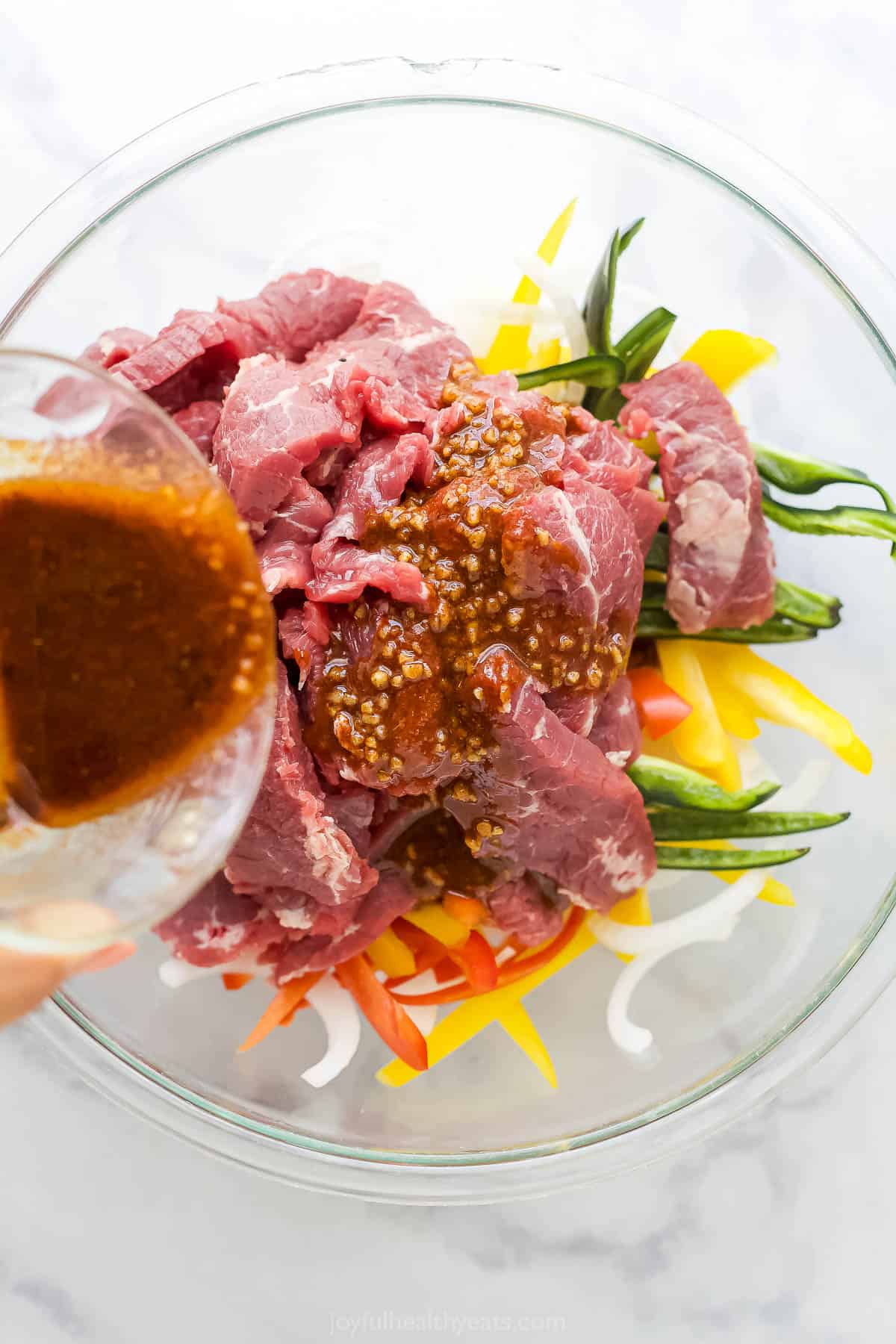 Pouring the seasoning mixture over the steak and veggies in a bowl. 