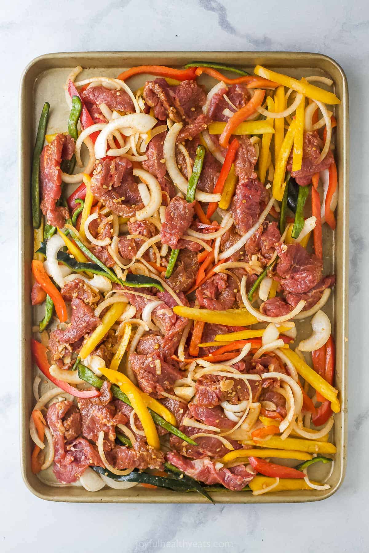 Uncooked beef fajitas on baking sheet. 