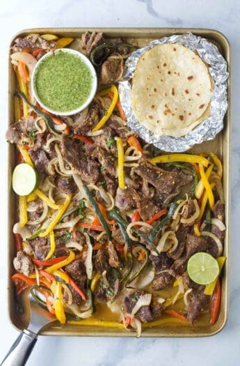 Sheet pan steak fajitas with cilantro chimichurri and flour tortillas on the side.