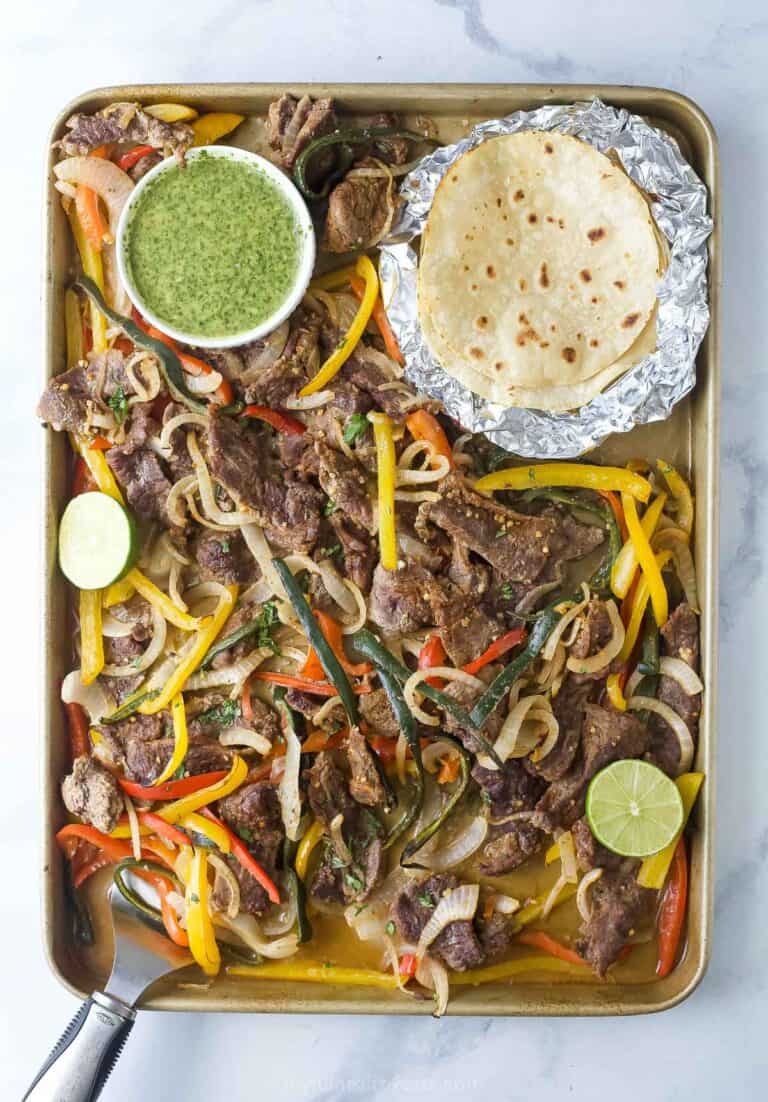 Sheet pan steak fajitas with cilantro chimichurri and flour tortillas on the side.