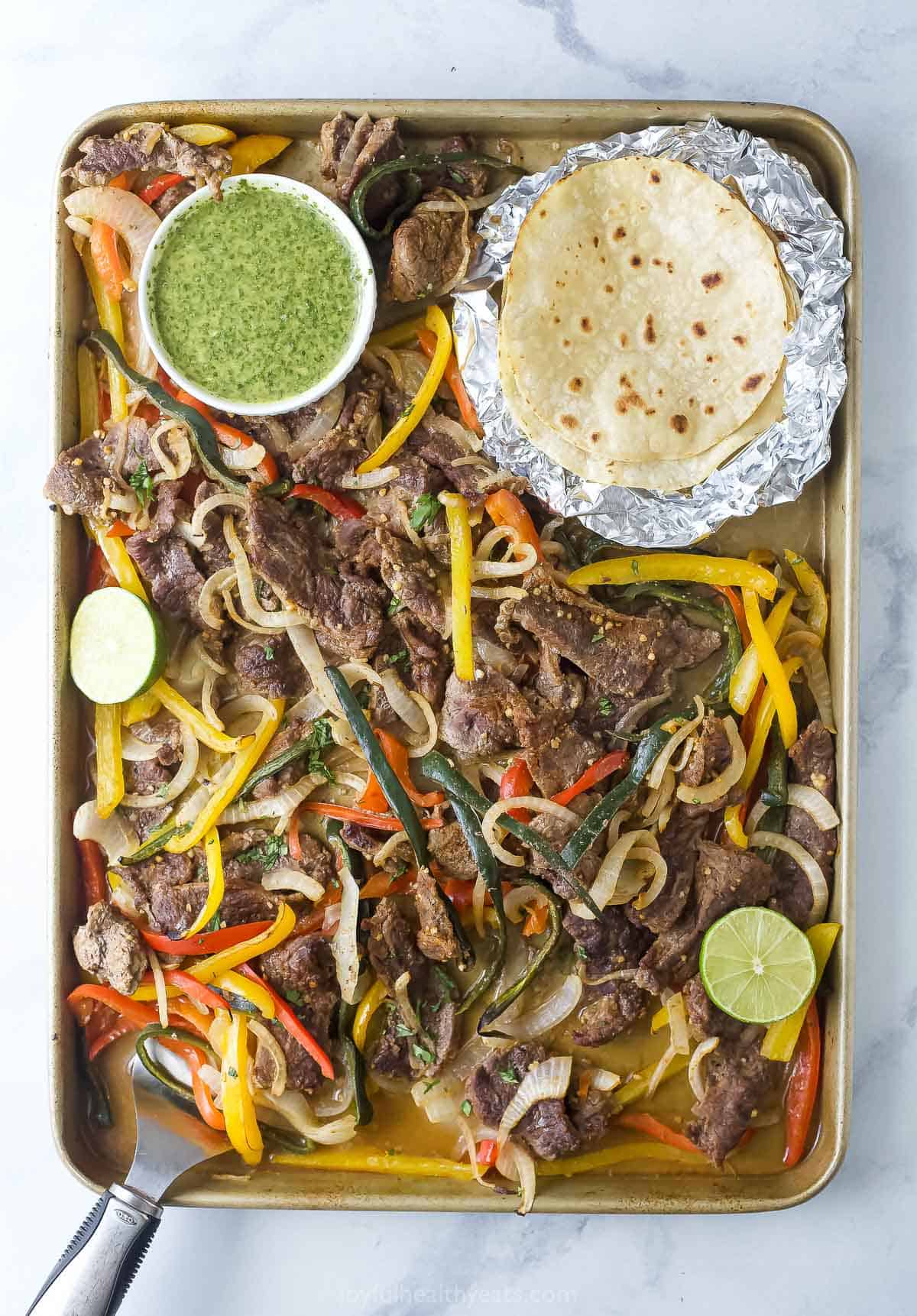 Sheet pan steak fajitas with cilantro chimichurri and flour tortillas on the side. 