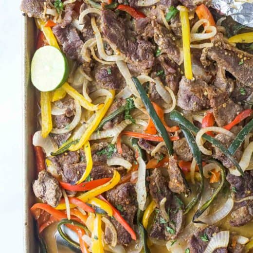 Homemade beef fajitas with bell peppers, poblanos, and onions in a baking sheet.