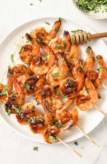 Plate of honey garlic shrimp skewers with cilantro on top.