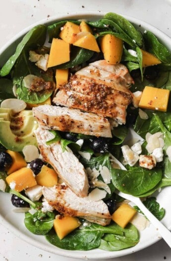 Bowl of avocado salad with mango, blueberries, grilled chicken, and goat cheese.