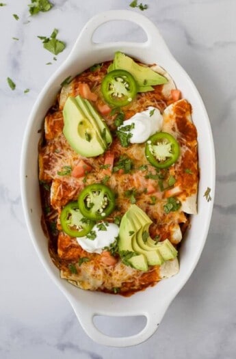 Cheesy Tex-Mex enchiladas with sour cream, jalapeños, cilantro, and avocado on top.