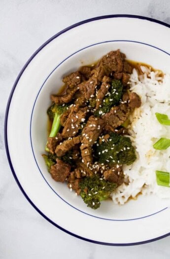 Saucy Instant Pot Mongolian beef in a bowl with fluffy rice and green onions.