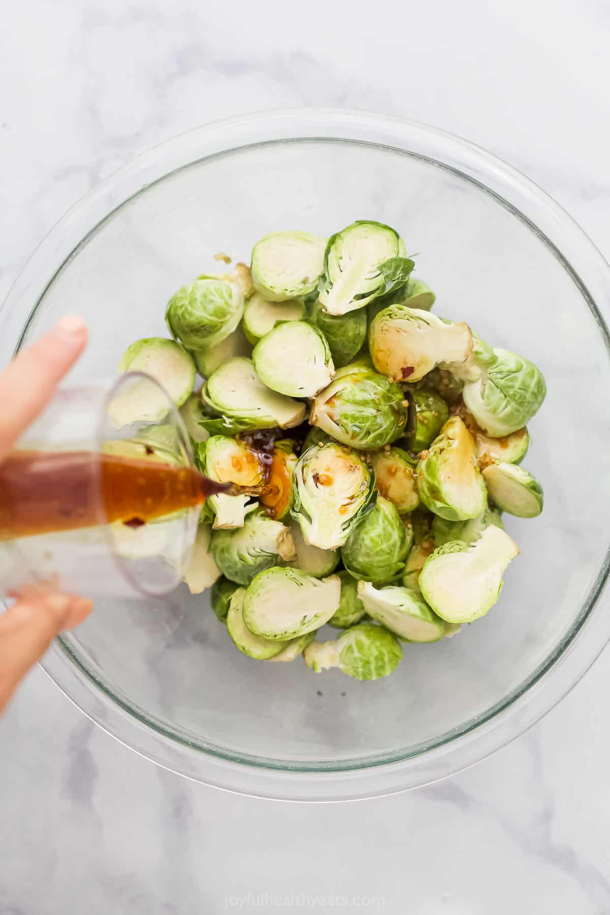 Pouring the soy sauce glaze over the Brussels sprouts in a glass bowl. 