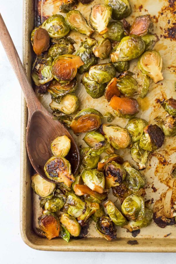 Grabbing some honey-soy sauce Brussels sprouts from the baking sheet with a wooden spoon.