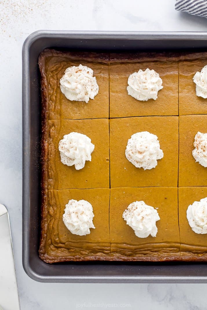 pumpkin pie bars in a baking dish topped with almond milk whipped cream