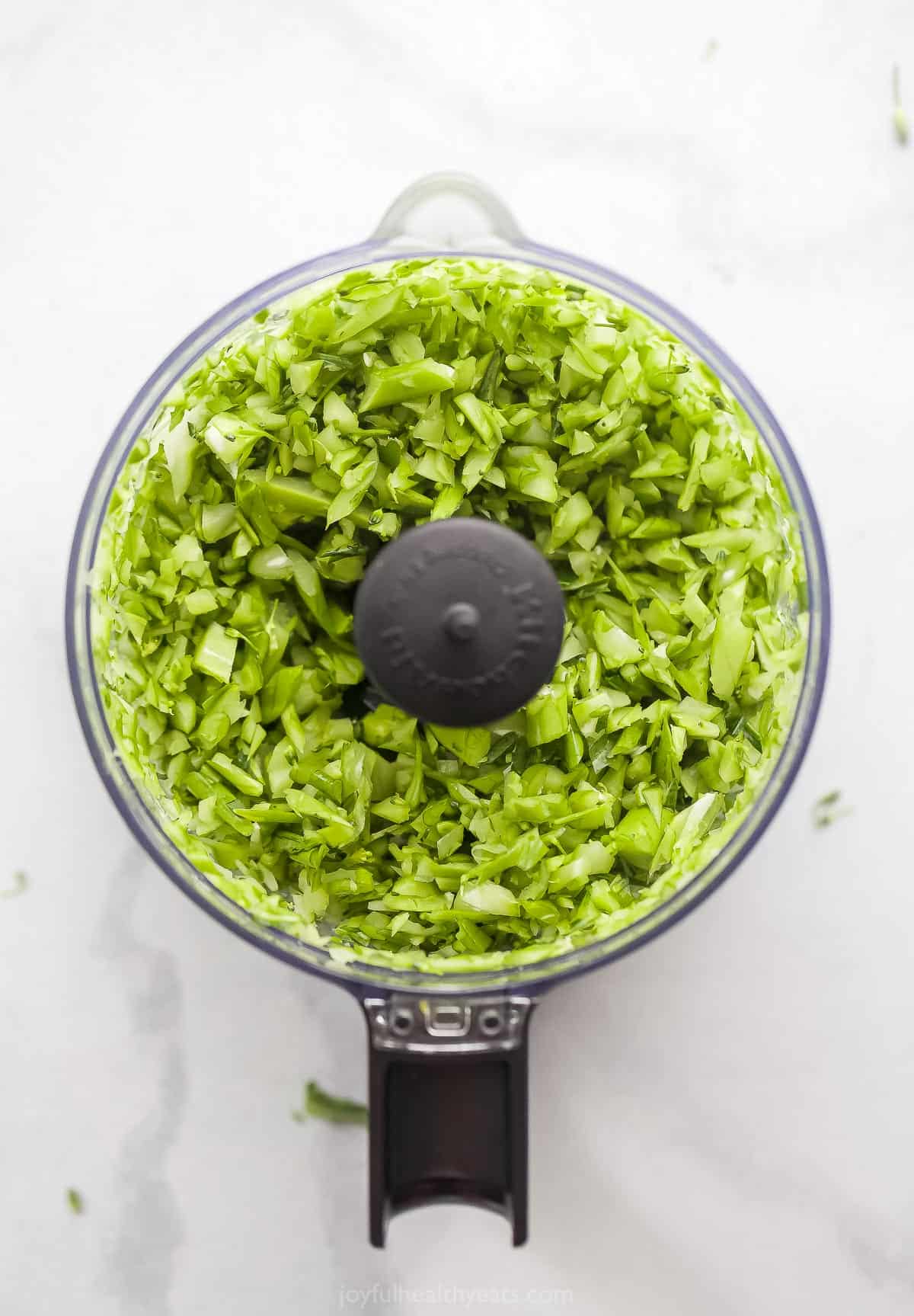 Chopped broccolini stems inside of a food processor on a kitchen countertop