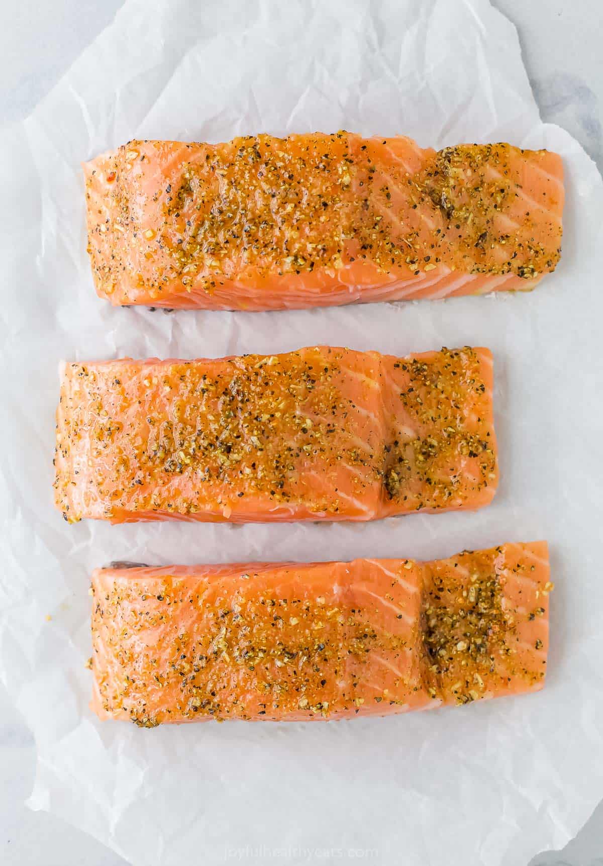 Three seasoned salmon fillets on a sheet of parchment paper