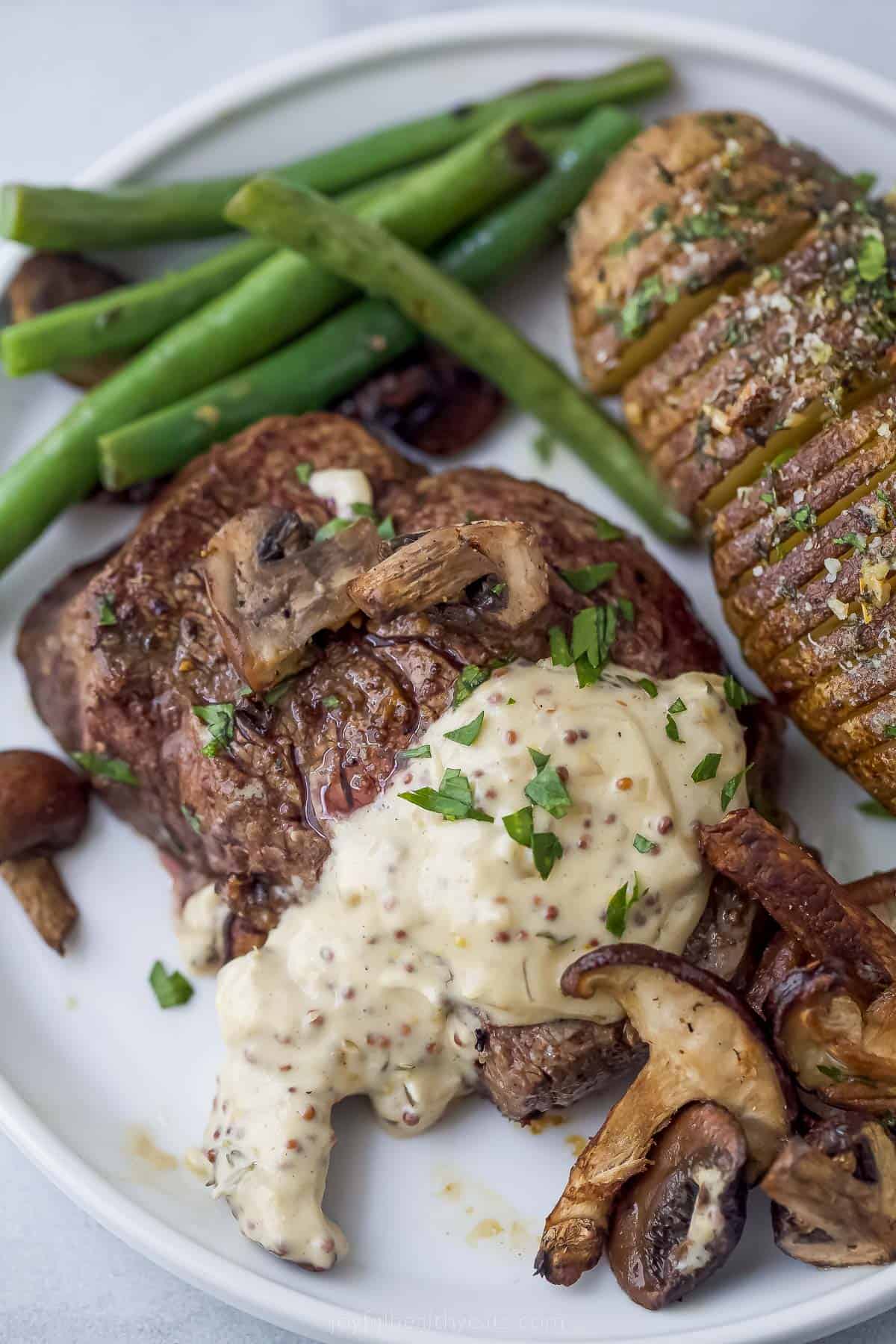 filet mignon with mustard and mushrooms on a plate with potato and green beans
