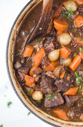 a pot of beef bourguignon with carrots, pearl onions, and mushrooms in a dark gravy