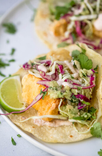 a fish taco on a plate with lime garnish and slaw on top