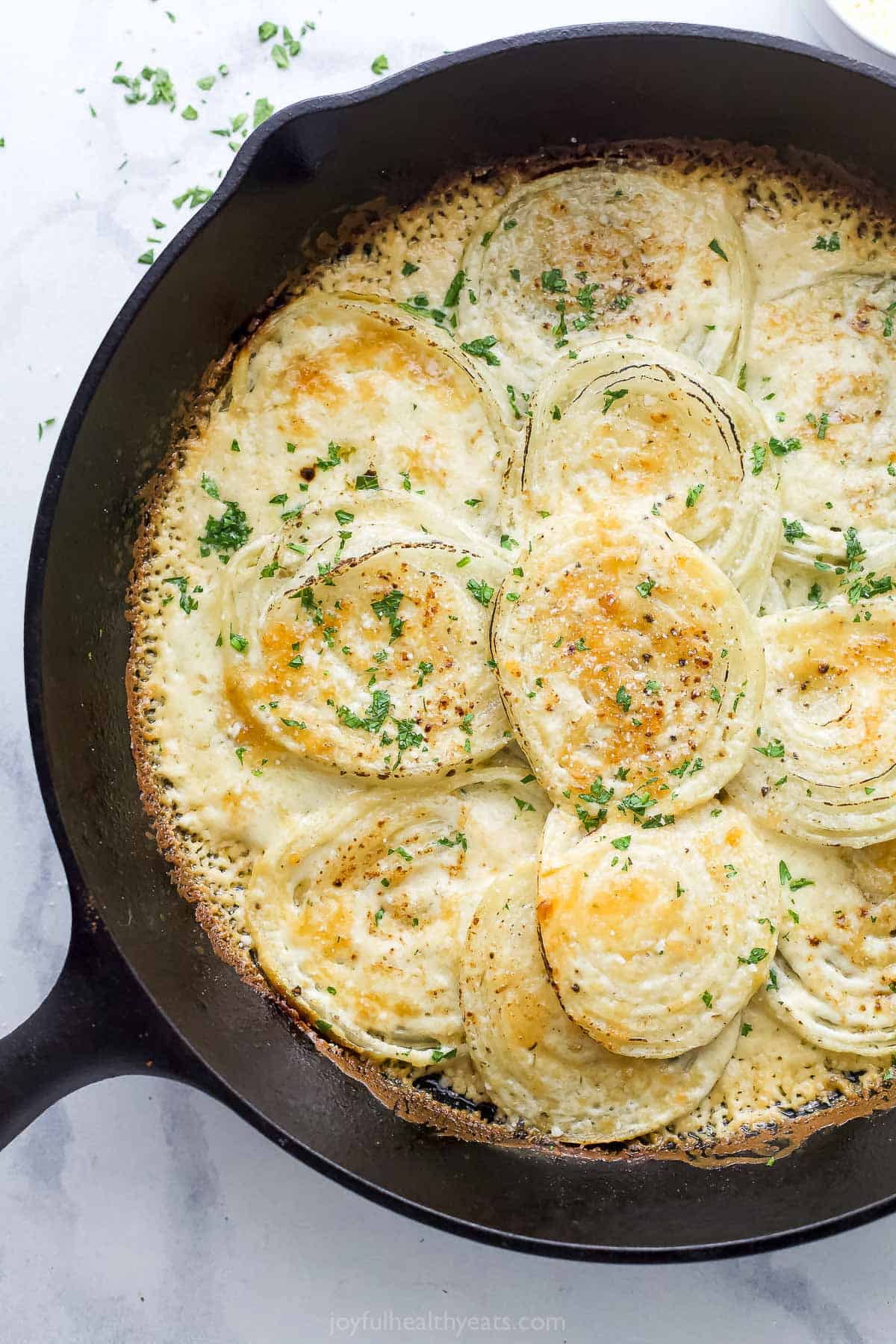 Angled photo of creamed onions with melty cheese and a fresh parsley garnish.