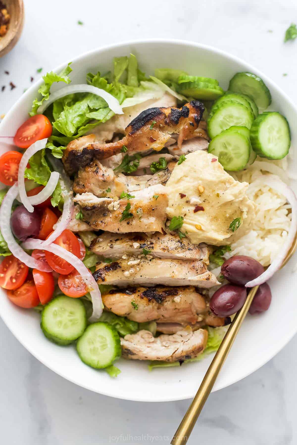 Greek chicken bowls with hummus, veggies, rice, and Greek vinaigrette. 