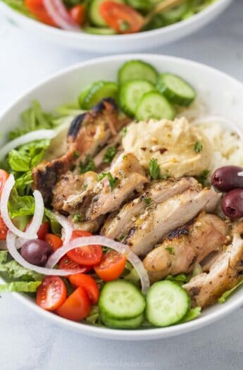 Close-up of the grilled chicken in these Greek-style bowls with veggies, rice, and hummus.