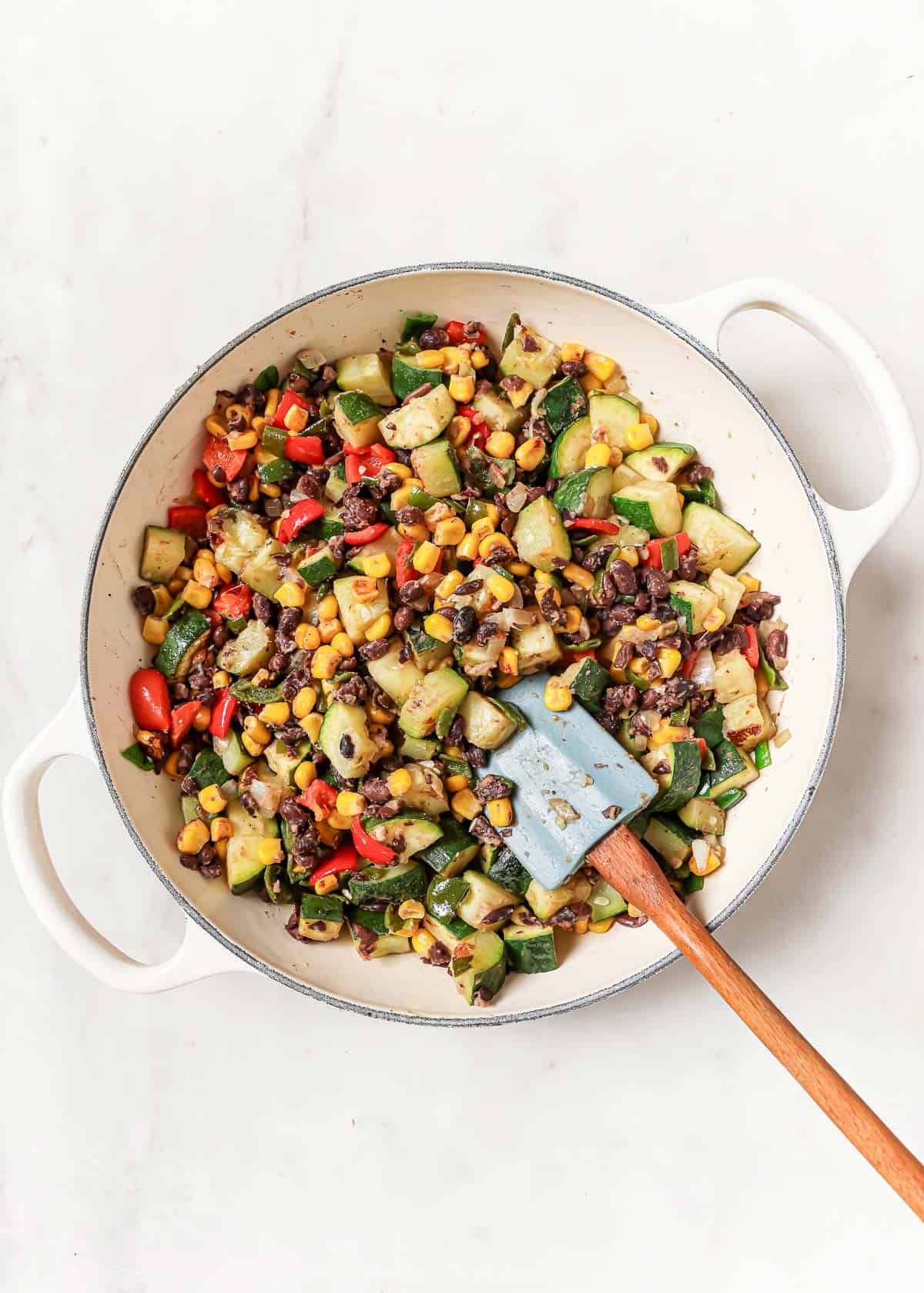 Mixing the sautéed veggie mixture with beans in the skillet. 