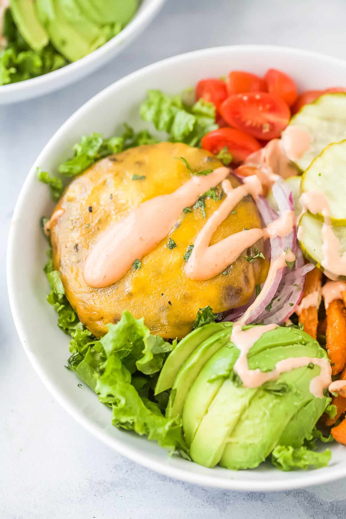 Angled photo of a burger bowl with melty cheese, avocado, tomatoes, onions, and pickles. 