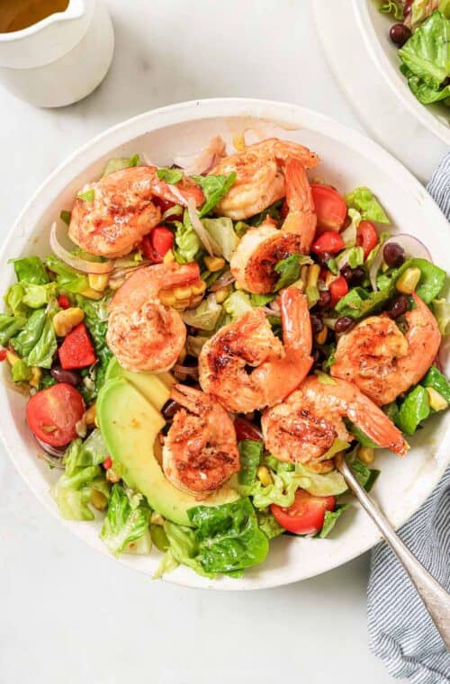 A bowl of grilled shrimp salad with creamy avocado, beans, and juicy tomatoes.