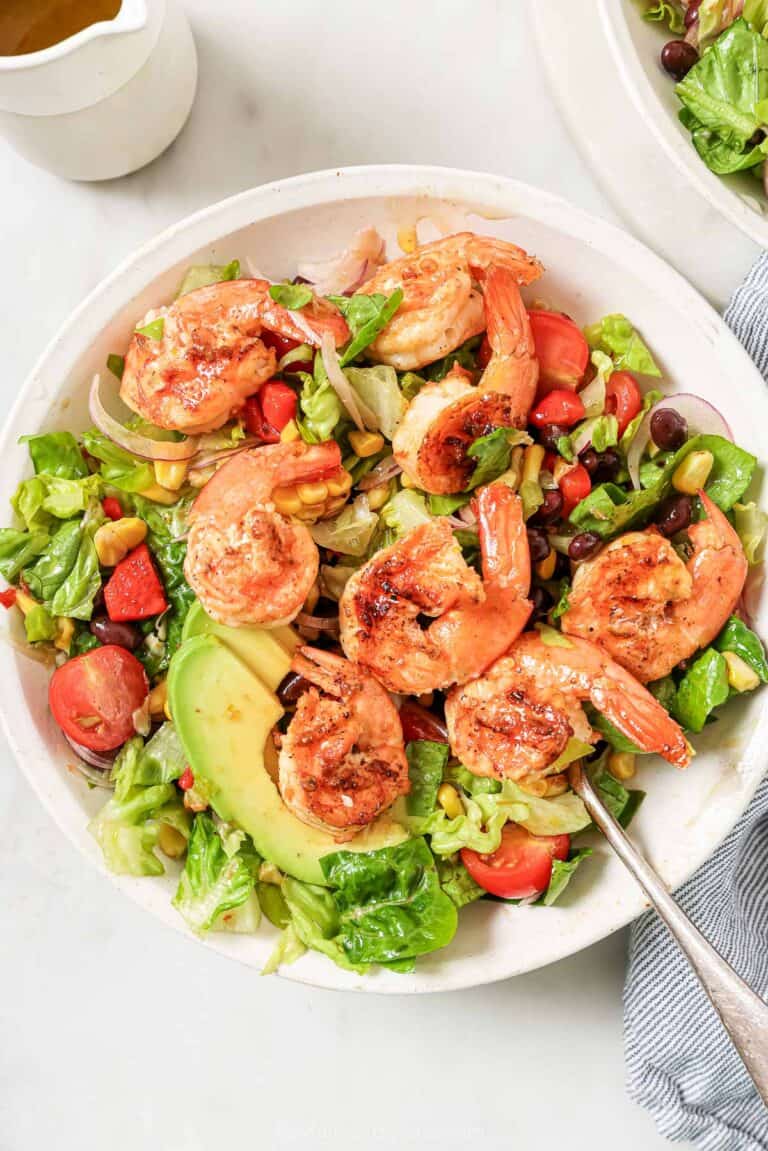 A bowl of grilled shrimp salad with creamy avocado, beans, and juicy tomatoes.