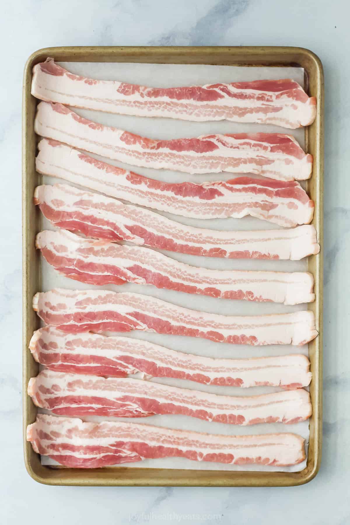 Raw bacon on the baking sheet. 